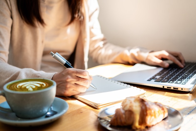 Młoda kobieta z filiżanką kawy siedzi i pracuje na laptopie w kawiarni