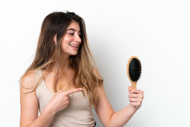 Młoda kobieta z grzebieniem do włosów na białym tle wskazująca na bok, aby zaprezentować produkt