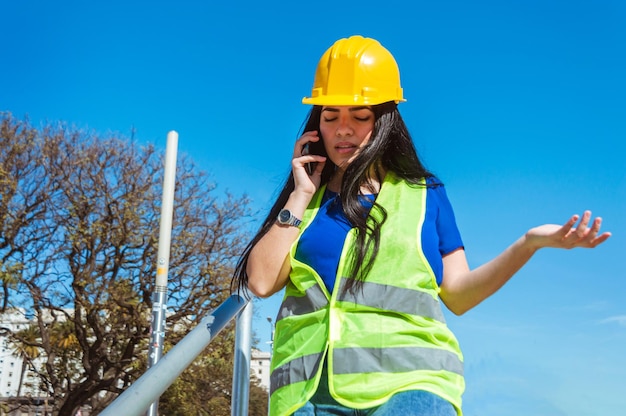 Młoda kobieta z kaskiem ochronnym na zewnątrz kłóci się przez telefon, gestykulując ręką