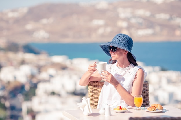 Młoda kobieta z kawą w kawiarni na świeżym powietrzu z niesamowitym widokiem na miasto Mykonos.