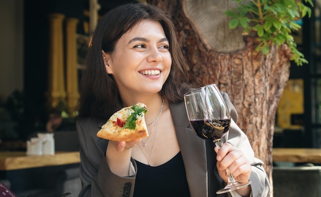 Młoda kobieta z kieliszkiem wina i kawałkiem pizzy w restauracji