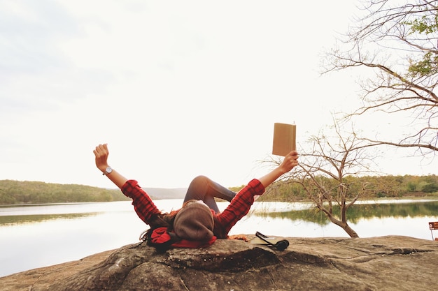 Zdjęcie młoda kobieta z książką leżąca na skale nad jeziorem na tle nieba
