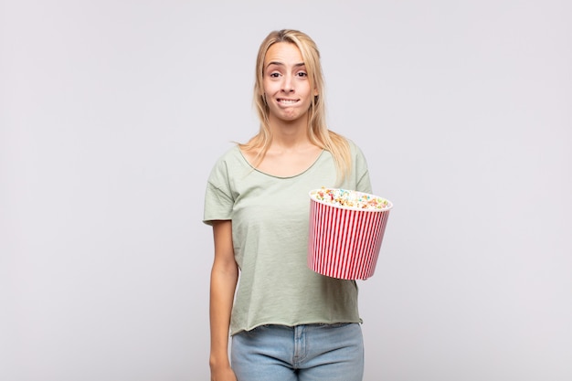 Młoda Kobieta Z Kubełkiem Popcornów Wyglądająca Na Zdziwioną I Zdezorientowaną, Przygryzając Wargę Nerwowym Gestem, Nie Znając Odpowiedzi Na Problem