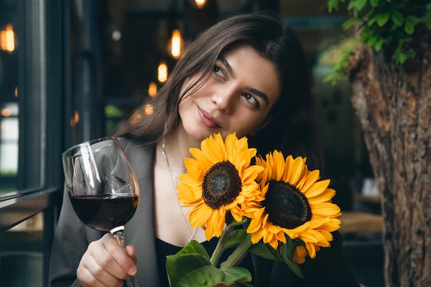 Młoda kobieta z lampką wina i bukietem słoneczników w restauracji