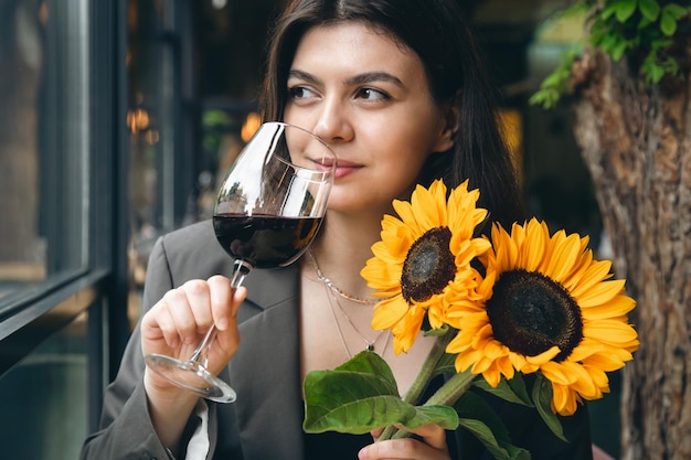 Młoda kobieta z lampką wina i bukietem słoneczników w restauracji