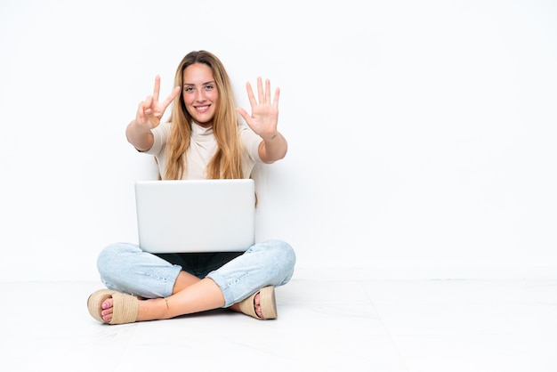Młoda kobieta z laptopem siedzi na podłodze na białym tle, licząc siedem palcami