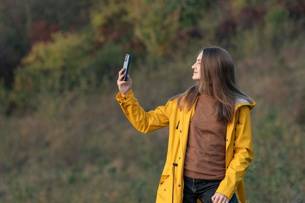 Młoda kobieta z lasem smartfona na tle Dziewczyna w żółtej kurtce photographe o jesiennej naturze