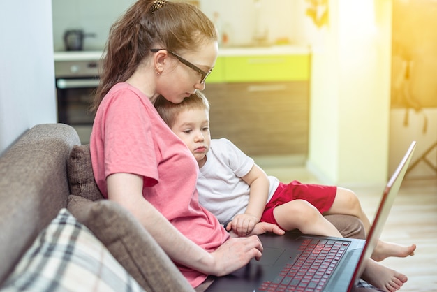 Młoda Kobieta Z Małym Dzieckiem Na Kolanach Siedzi Przy Laptopie