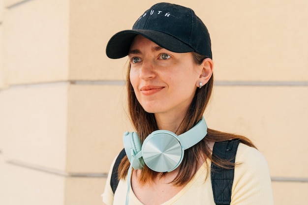 Młoda kobieta z miętowymi słuchawkami i czarną czapką na ulicy