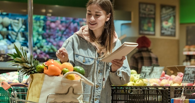 Młoda Kobieta Z Notatnikiem Kupuje Artykuły Spożywcze W Supermarkecie.