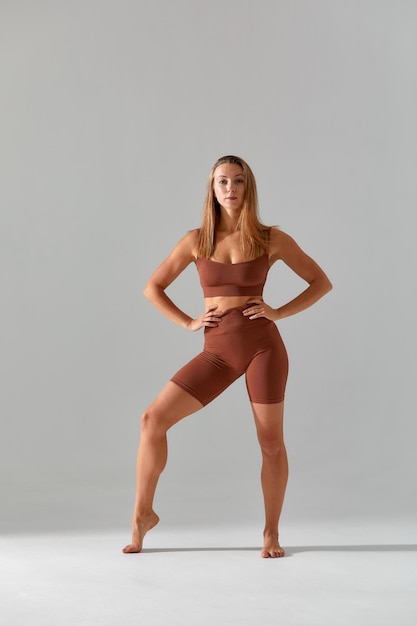 Młoda kobieta z pięknym szczupłym zdrowym ciałem pozuje w studio Fitness modelki w odzieży sportowej na szarym tle