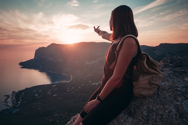 Młoda kobieta z plecakiem cieszy się widokiem na góry i morze o zachodzie słońca. Styl życia koncepcja emocjonalna wakacje weekendowy wypad z lotu ptaka Krymski krajobraz