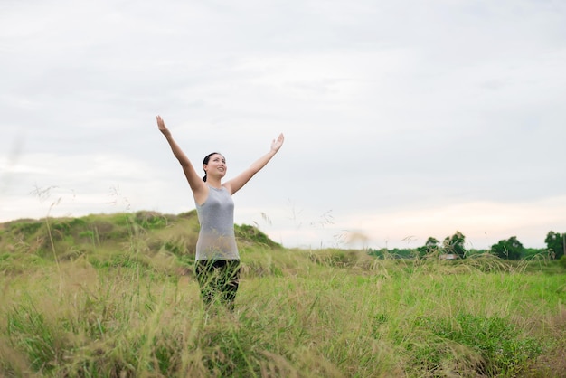 Zdjęcie młoda kobieta z podniesionymi ramionami stojąca na trawiastym polu przeciwko niebu