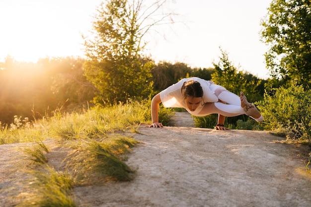 Młoda kobieta z rozciągającym się ciałem, ćwicząca jogę i wykonująca „Eight Angle Pose” na zewnątrz w parku