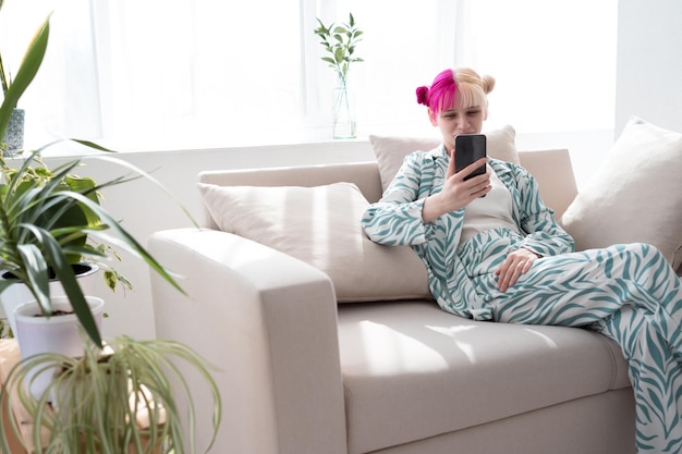 Młoda kobieta z różowo-białymi włosami prowadzi rozmowę wideo za pomocą smartfona w domu