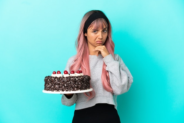 Młoda kobieta z różowymi włosami trzyma tort urodzinowy na białym tle na myślenie o niebieskim tle