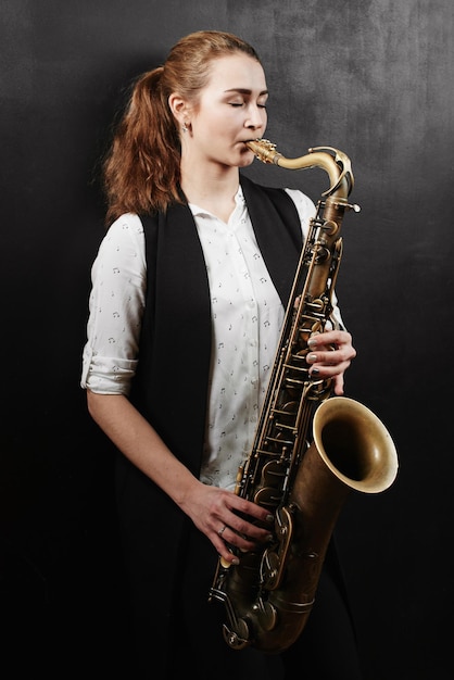 Młoda kobieta z saksofonem na czarnym tle