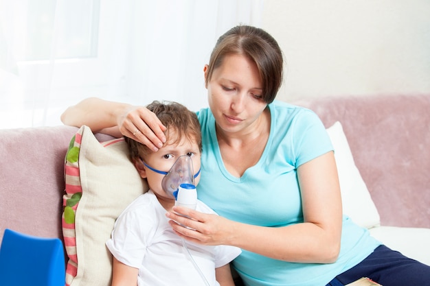 Młoda kobieta z synem robi inhalację z nebulizatorem w domu i czyta książkę