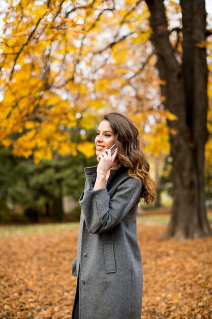 Młoda kobieta z telefonem komórkowym w jesień parku