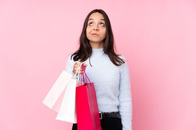 Młoda kobieta z torbą na zakupy na pojedyncze różowe ściany i patrząc w górę