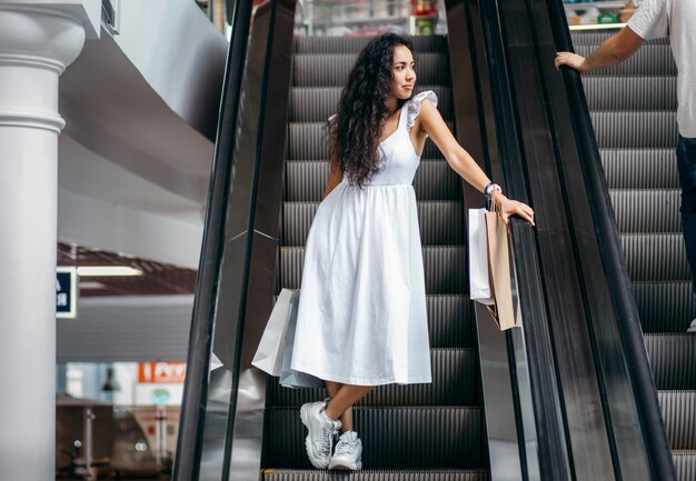 Młoda kobieta z torbami na schodach ruchomych