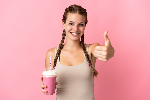 Zdjęcie młoda kobieta z truskawkowym koktajlem mlecznym na białym tle na różowej ścianie z kciukami do góry, ponieważ stało się coś dobrego