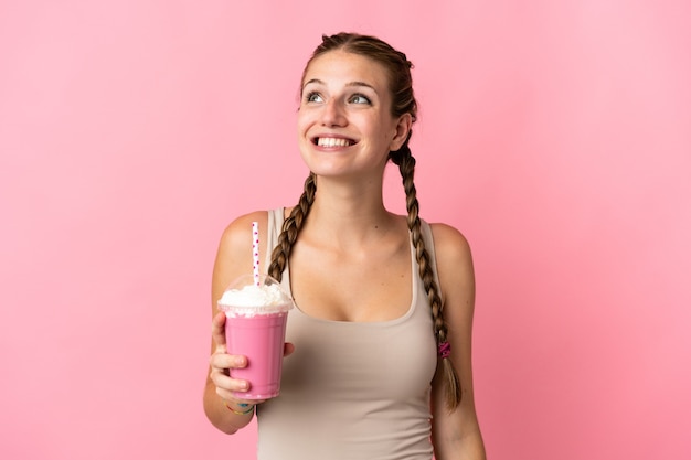 Młoda kobieta z truskawkowym koktajlem na białym tle na różowej ścianie myśli pomysł, patrząc w górę