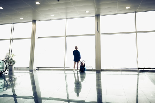 Młoda kobieta z walizką patrząca na duże okna na lotnisku airport