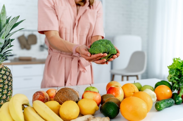 Młoda kobieta z warzywami trzyma brokuły w rękach gotowanie w kuchni. Stół ze zdrową żywnością. Przycięte zdjęcie.