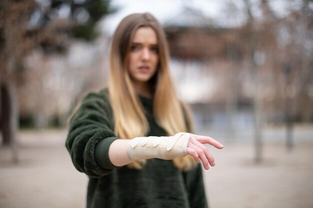 Zdjęcie młoda kobieta z złamaną ręką stoi na ulicy.