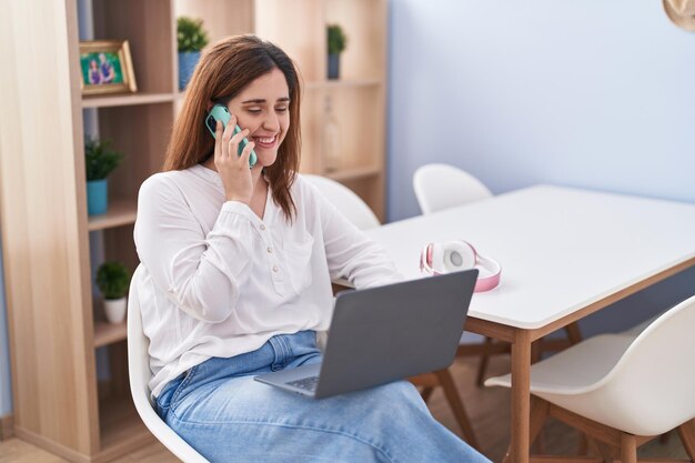 Młoda kobieta za pomocą laptopa i rozmowy na smartfonie w domu