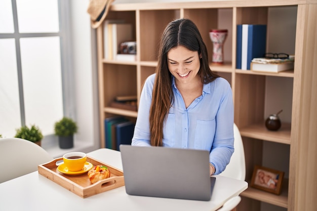 Młoda kobieta za pomocą laptopa o śniadanie w domu