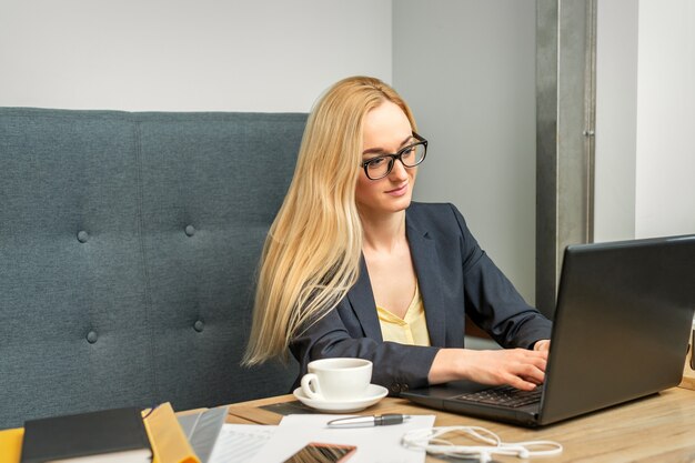 Młoda kobieta za pomocą laptopa siedząc przy stole w kawiarni