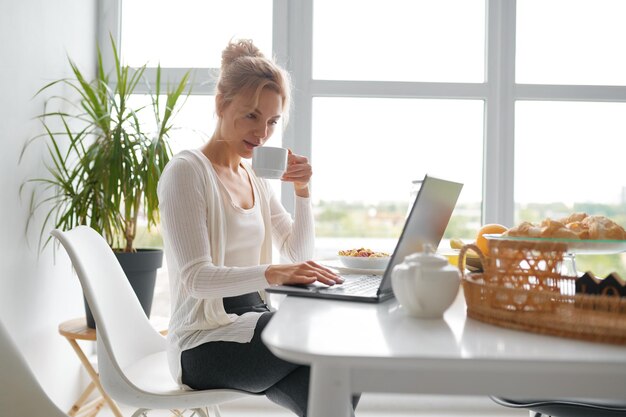 Młoda kobieta za pomocą laptopa w domowej kuchni