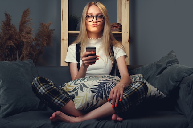 Młoda kobieta za pomocą telefonu komórkowego. Siedząc na kanapie. Koncepcja pozostania w domu podczas koronawirusa COVID-2019. Ścieśniać.
