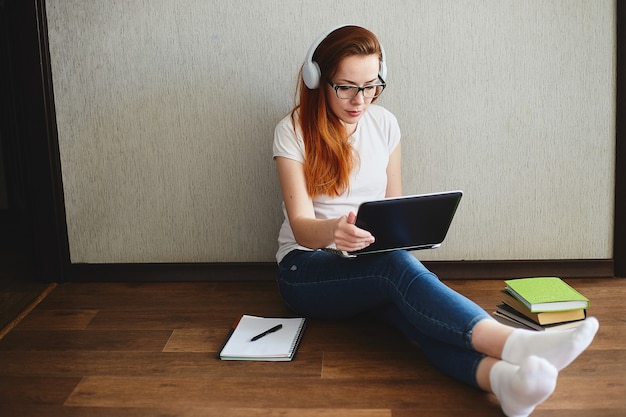 Młoda Kobieta Ze Słuchawkami Pracować Lub Uczyć Się Na Laptopie Siedząc Na Podłodze W Domu. Koncepcja Biura Domowego. Praca W Domu