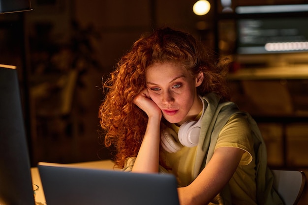 Młoda kobieta zmęczona pracą na komputerze, pracuje w terminie w ciemnym biurze