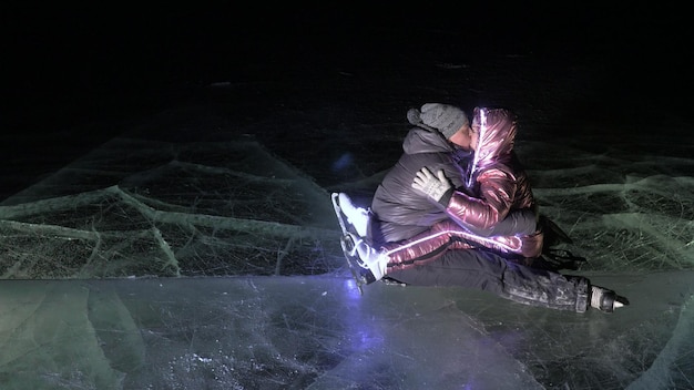 Młoda kochająca para jeździ na łyżwach na lodowisku w nocy Mężczyzna i kobieta całują się, przytulają się, bawią się, uczą się jeździć na łyżwach Uprawianie miłości na lodzie Piękny czysty lód z pęknięciami na jeziorze Lód podświetlany od dołu