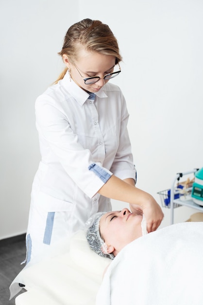 Młoda kosmetolog oczyszcza twarz pacjentkiZabieg upiększający na twarzKosmetologia