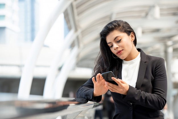 Młoda Łacińska biznesowa kobieta używa smartphone outdoors