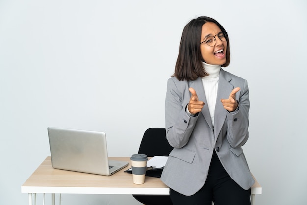 Młoda łacińska Kobieta Biznesu Pracująca W Biurze Na Białym Tle Wskazująca Do Przodu I Uśmiechnięta