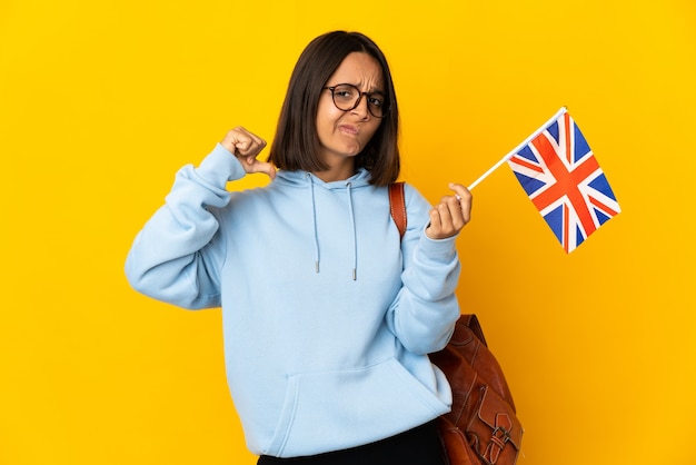 Młoda Łacińska kobieta trzyma flagę Wielkiej Brytanii na białym tle na żółtym tle dumna i zadowolona z siebie