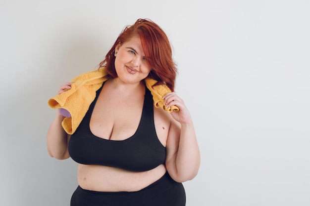 Młoda Łacińska plus size kobieta szczęśliwy uśmiechający się trzymając żółty ręcznik z rękami na białym tle