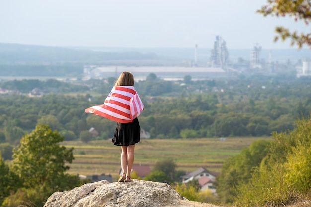 Młoda ładna Amerykańska Kobieta Z Długimi Włosami Trzyma Macha Na Wietrze Flaga Usa Na Jej Sholders Stojąc Na Zewnątrz, Ciesząc Się Ciepłym Letnim Dniem