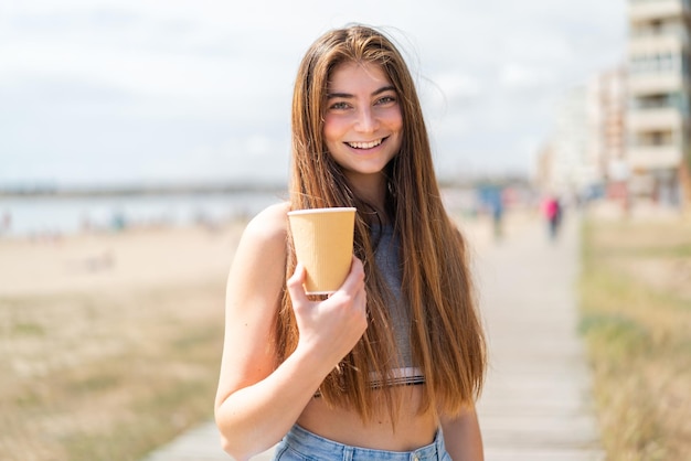 Młoda, ładna, biała kobieta trzymająca kawę z szczęśliwym wyrazem twarzy.