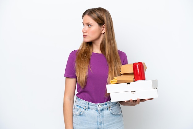 Młoda ładna blond kobieta trzyma fast food na białym tle patrząc w bok