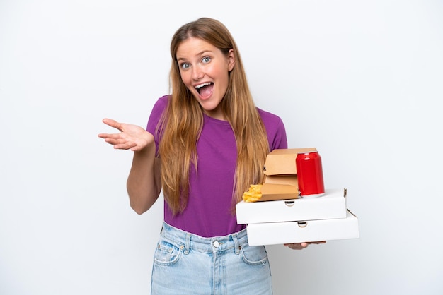 Młoda ładna blond kobieta trzyma fast food na białym tle z wstrząśniętym wyrazem twarzy