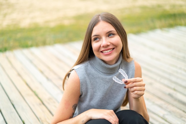 Młoda ładna blondynka trzyma niewidzialne szelki na zewnątrz, patrząc w górę, uśmiechając się