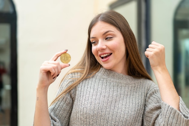 Młoda ładna blondynka trzymająca Bitcoina na zewnątrz świętująca zwycięstwo