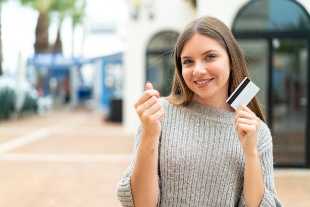 Młoda ładna blondynka trzymająca kartę kredytową robi gest pieniężny